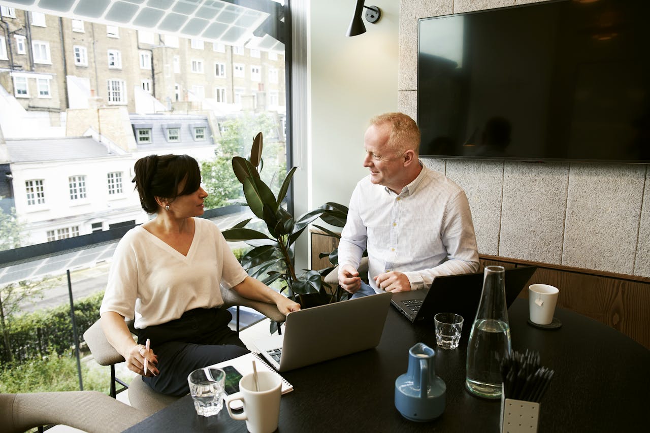 why-choose-us Two business professionals engaging in a team meeting in a modern London office with a large window view.